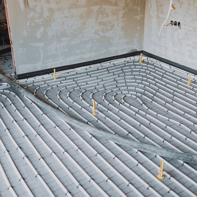 Chauffage au sol : Installation des tubes et de l'isolant Installation de chauffage au sol avec tubes blancs en serpentins sur isolant quadrillé en chantier.