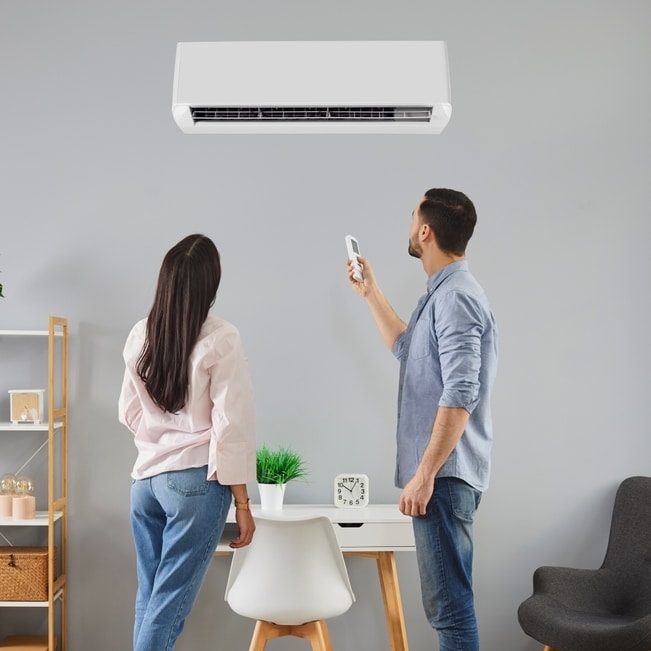 Réglage d'un climatiseur mural avec télécommande sans fil Couple utilisant une télécommande pour régler un climatiseur mural blanc dans un bureau à domicile moderne.