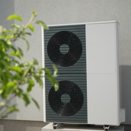 Pompe à chaleur air-eau : chauffage durable et efficace Pompe à chaleur air-eau moderne installée à l'extérieur contre un mur gris avec feuillage au premier plan.