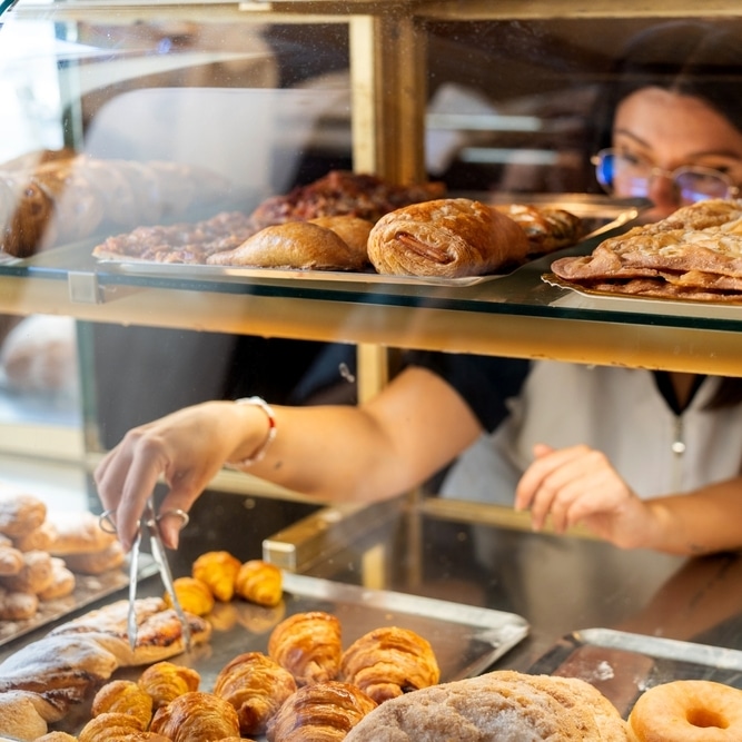 Viennoiseries Fraîches et Croissants en Vitrine de Boulangerie Boulangère servant des croissants et viennoiseries dorées dans une vitrine artisanale avec des pinces.